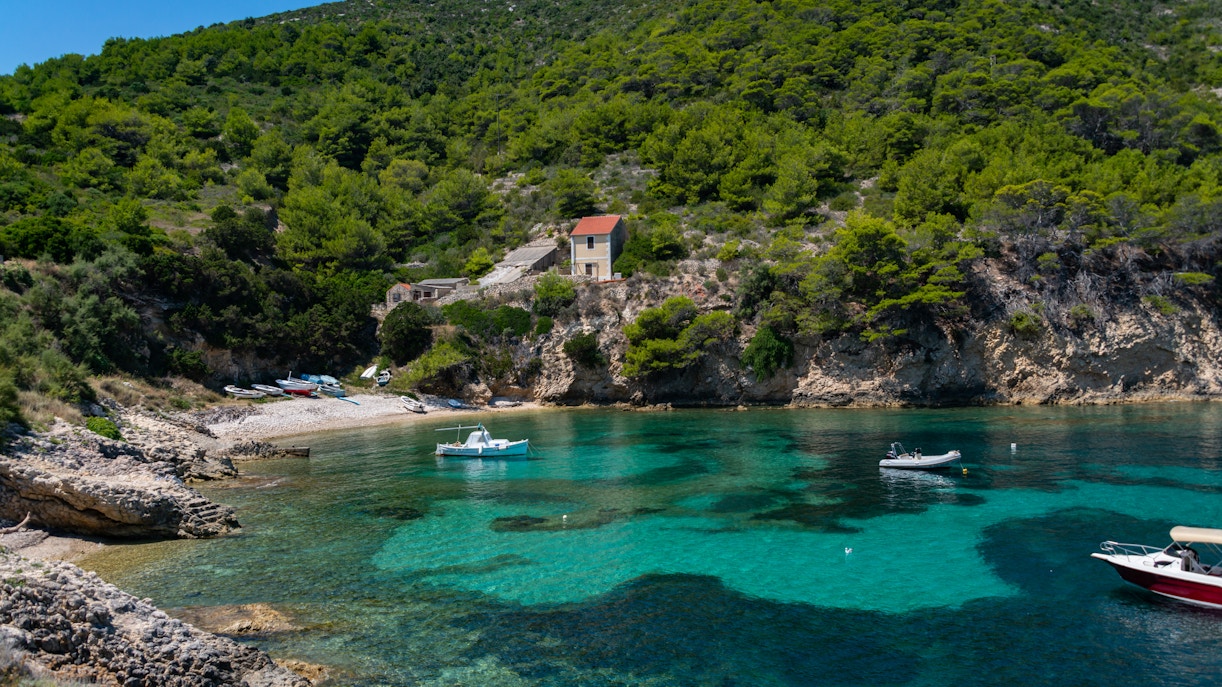 Boats anchored in a clear turquoise bay with a hillside and house on Biševo Island, Adriatic Sea.