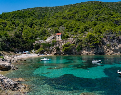 Boats anchored in a clear turquoise bay with a hillside and house on Biševo Island, Adriatic Sea.