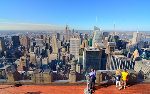 Visitors enjoying New York City skyline view from Top of the Rock, Empire State Building visible.