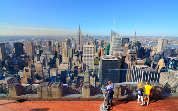 Visitors enjoying New York City skyline view from Top of the Rock, Empire State Building visible.