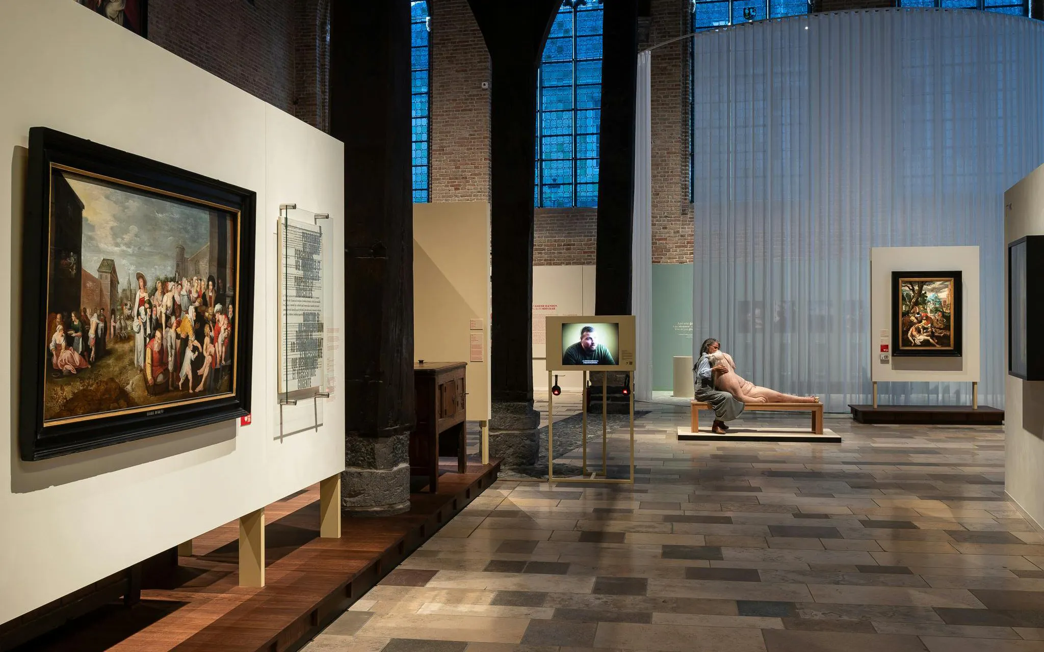 Museum Sint-Janshospitaal interior with paintings and visitor on bench.