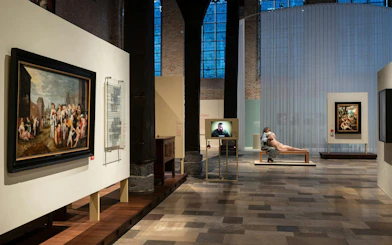Museum Sint-Janshospitaal interior with paintings and visitor on bench.