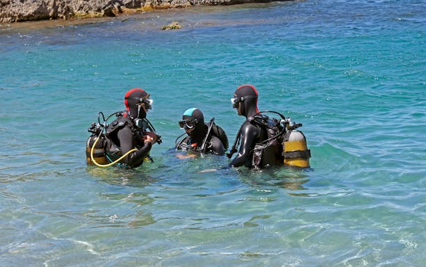 Instructor and students in wetsuits preparing for a dive in clear coastal waters.