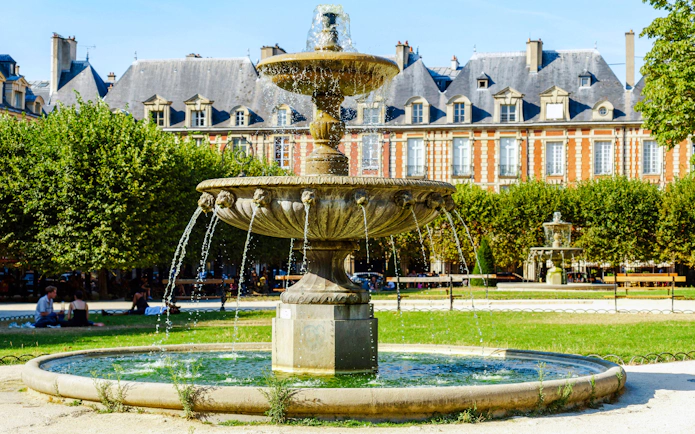 Fountain at Place des Vosges with historic buildings in Paris, France.
