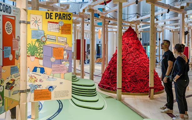 Exhibit at Paris museum with colorful educational panels and visitors observing a red art installation.