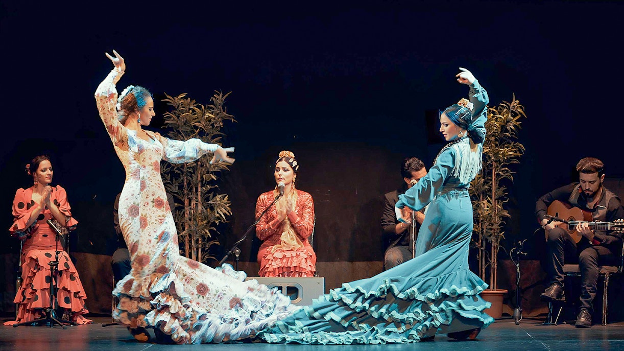 Dançarinos de flamenco em barcelona no palco, com trajes tradicionais, iluminados por luzes vermelhas e azuis vibrantes.