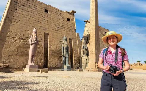 Woman holding a camera in front of Luxor Temple statues and obelisk, Egypt.