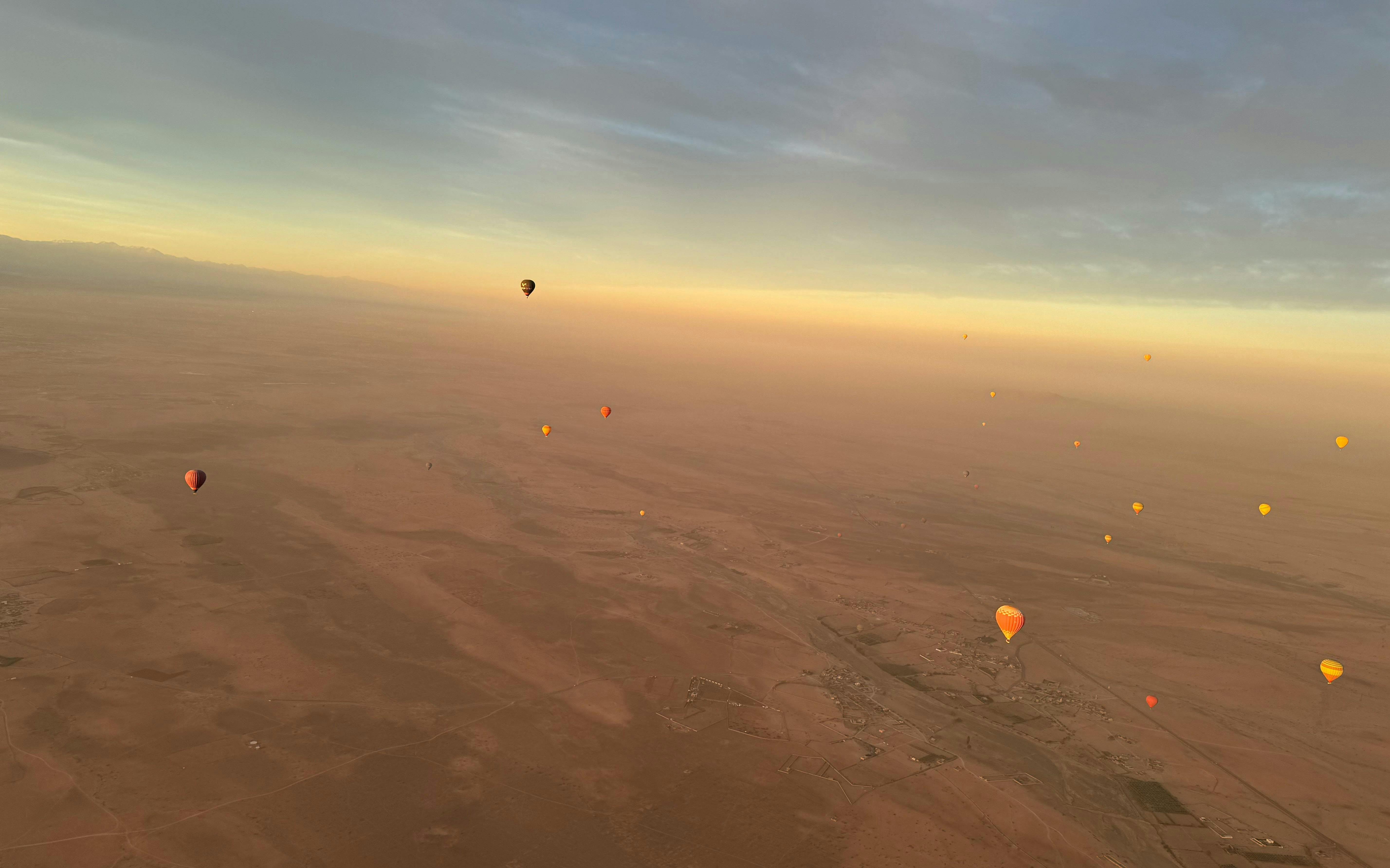 Hot air balloons floating over Marrakech desert at sunrise.