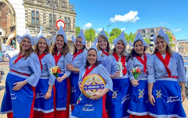 Women in traditional Dutch attire at Alkmaar Cheese Market, holding tulips and cheese wheel.