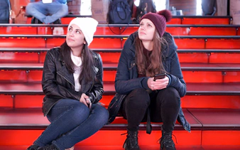 Two girls sitting on the red steps at Times Square at night.