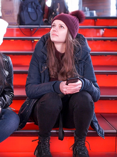 Two girls sitting on the red steps at Times Square at night.