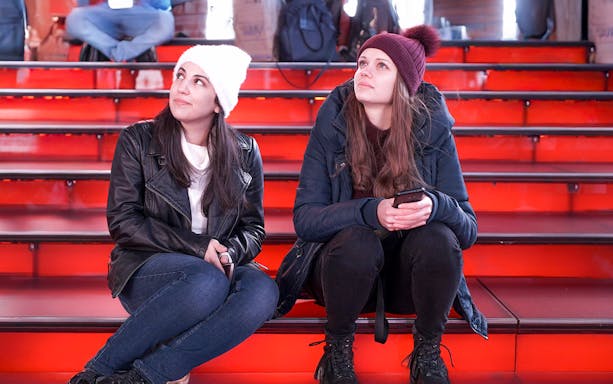 Two girls sitting on the red steps at Times Square at night.
