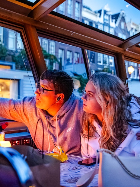 Guests enjoying a winter evening cruise in Amsterdam, taking photos through the boat window.