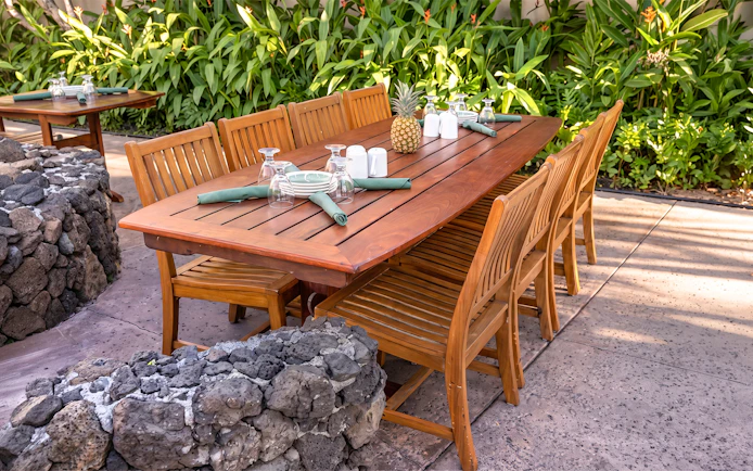 Outdoor dining setup at Old Lahaina Luau with wooden table, chairs, and tropical decor.