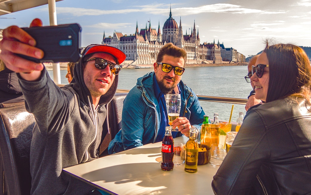 Group enjoying drinks on a Budapest party boat cruise with the Hungarian Parliament in the background.