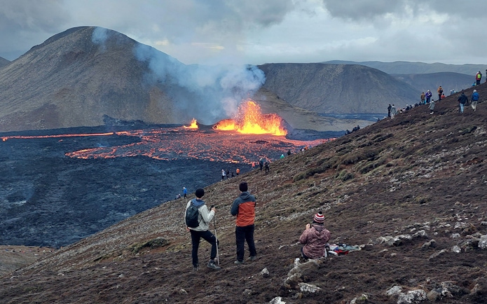 Hikers observing volcanic eruption and lava flow in Reykjanes, Iceland.
