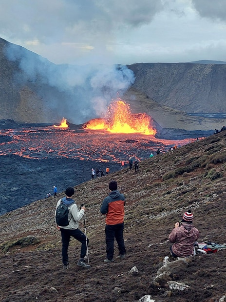 Hikers observing volcanic eruption and lava flow in Reykjanes, Iceland.