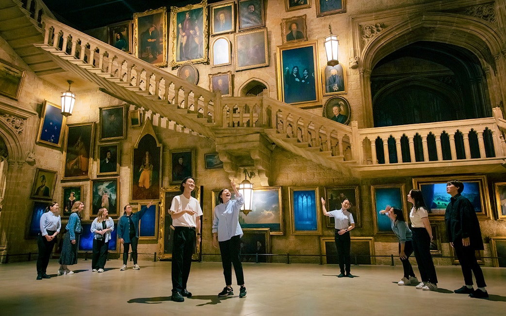 Visitors at Warner Bros. Studio Tour Tokyo exploring Hogwarts staircase and portraits.