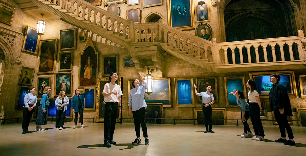 Visitors at Warner Bros. Studio Tour Tokyo exploring Hogwarts staircase and portraits.