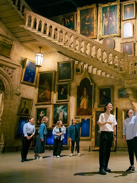 Visitors at Warner Bros. Studio Tour Tokyo exploring Hogwarts staircase and portraits.