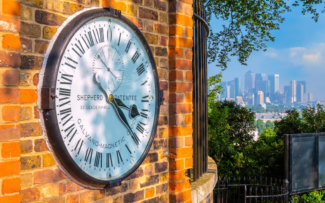 Shepherd Gate Clock at Royal Observatory Greenwich with London skyline in background.