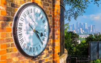 Shepherd Gate Clock at Royal Observatory Greenwich with London skyline in background.