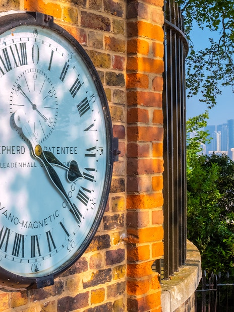 Shepherd Gate Clock at Royal Observatory Greenwich with London skyline in background.