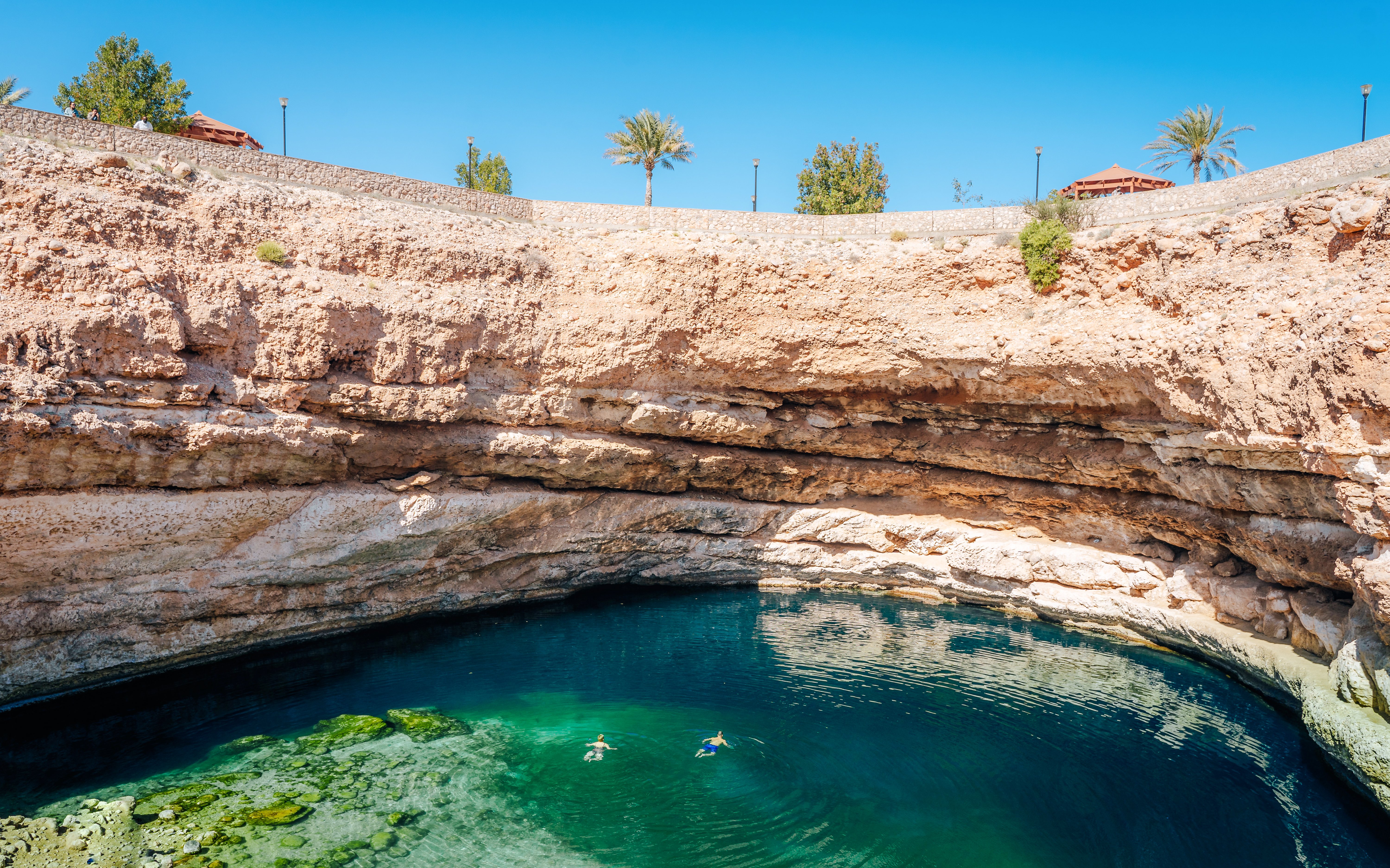 Swimmers in Bimmah Sinkhole's turquoise waters, Oman.