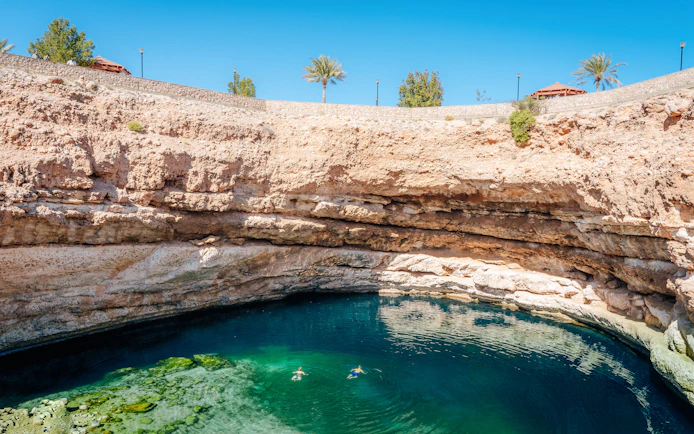 Swimmers in Bimmah Sinkhole's turquoise waters, Oman.