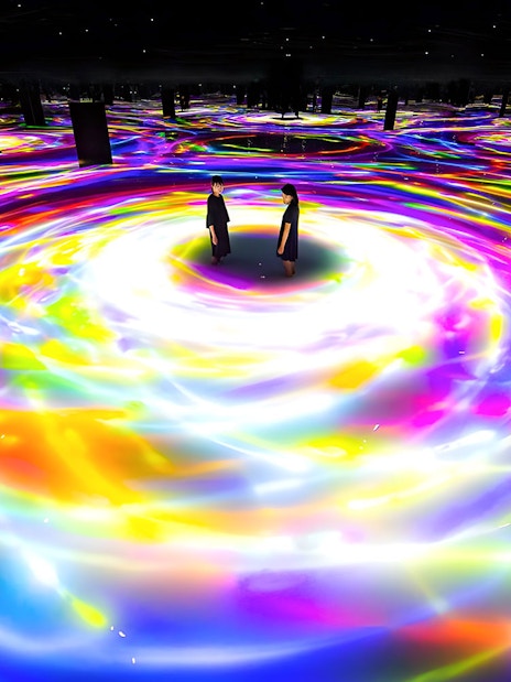 Visitors standing in colorful digital art installation at TeamLab Planets, Tokyo.