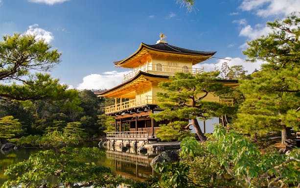 Kinkaku-ji Temple in Kyoto surrounded by trees and reflecting in a pond.