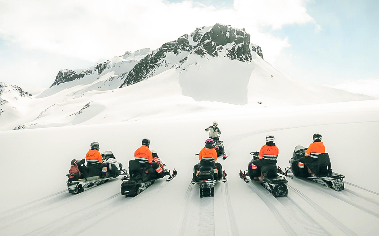 Snowmobile riders on Langjökull Glacier with snowy mountain backdrop.