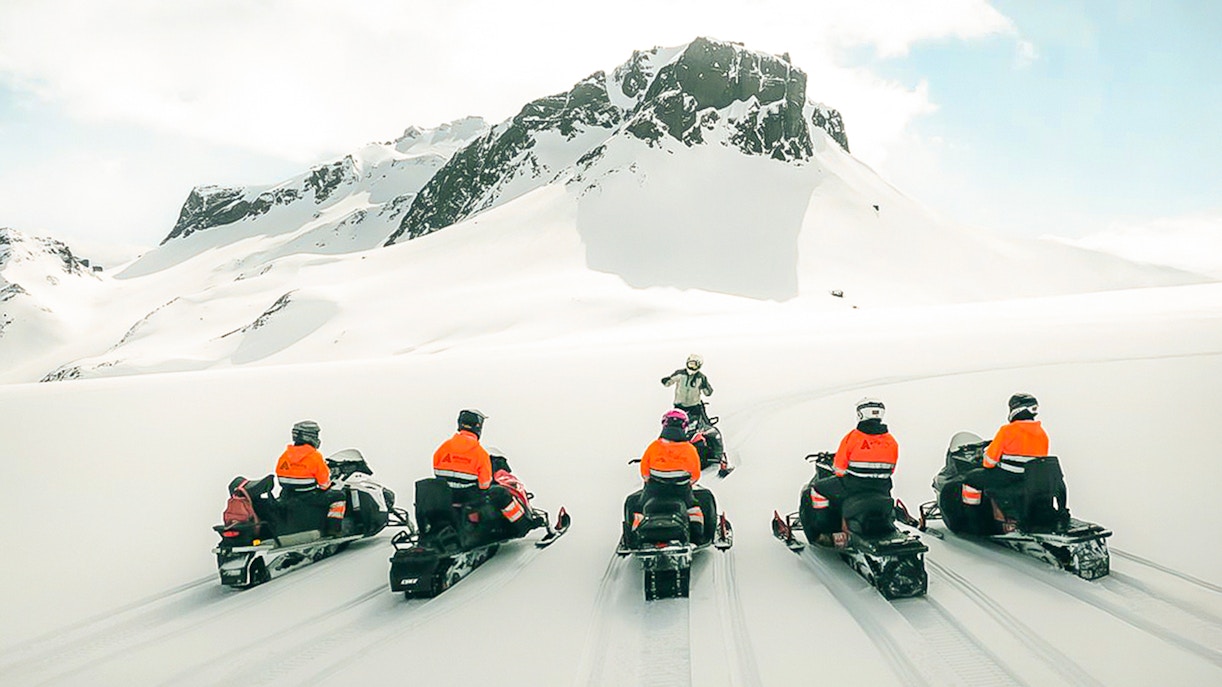 Snowmobile riders on Langjökull Glacier with snowy mountain backdrop.