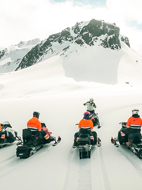 Snowmobile riders on Langjökull Glacier with snowy mountain backdrop.