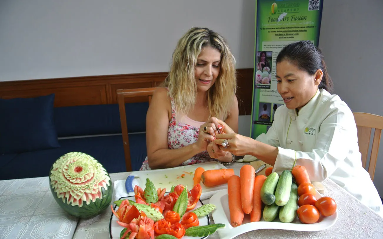 Master carver teaching fruit and vegetable carving in Thai class with carved watermelon and fresh produce.