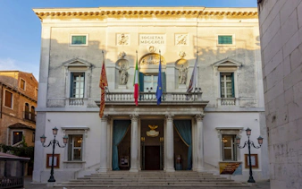 Facade of Teatro La Fenice in Venice with flags and statues, part of the Holy Heist city exploration game.