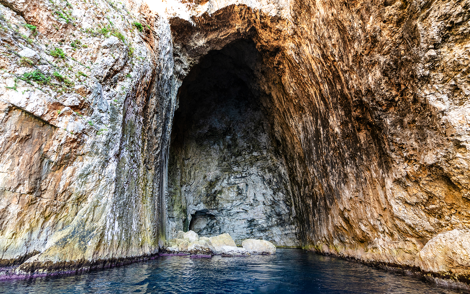 Haxhi Ali Cave entrance with rocky walls and blue water, Albania.