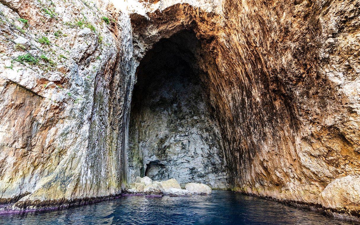 Haxhi Ali Cave entrance with rocky walls and blue water, Albania.