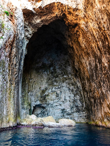 Haxhi Ali Cave entrance with rocky walls and blue water, Albania.