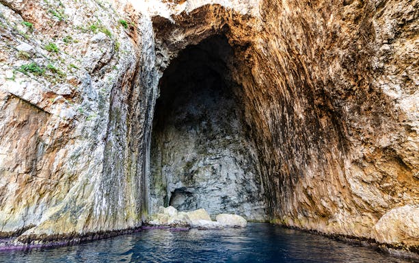 Haxhi Ali Cave entrance with rocky walls and blue water, Albania.