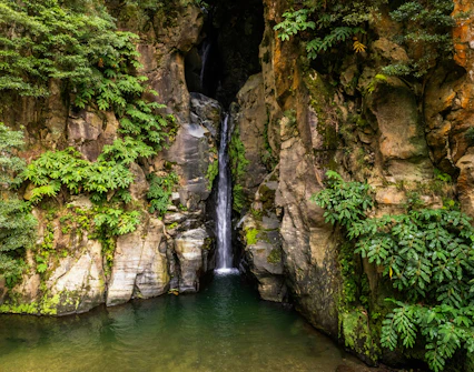 Salto do Cabrito Waterfall in Azores with rocky cliffs and lush green foliage.