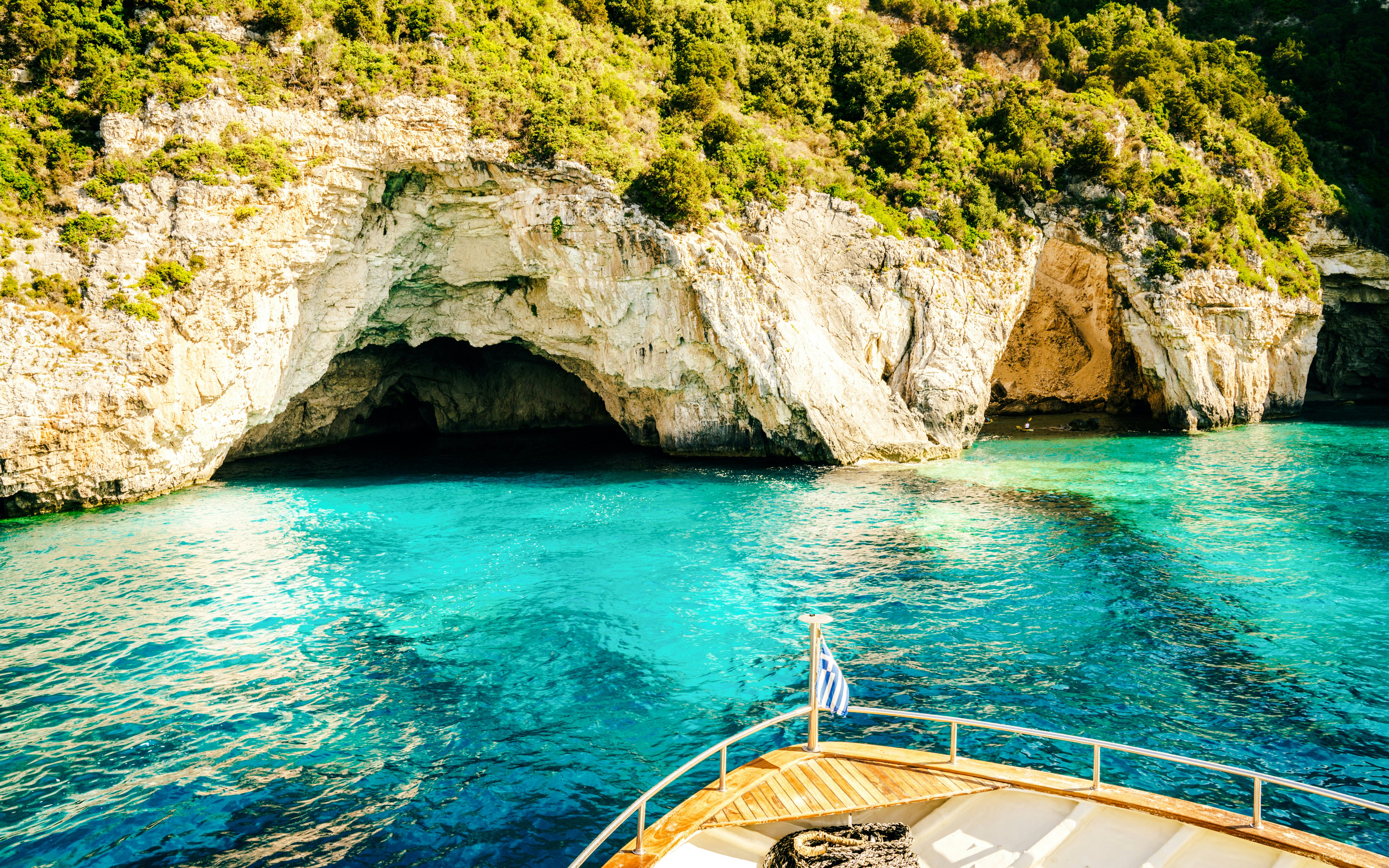 Boat approaching sea caves at Blue Lagoon, Corfu, with clear turquoise water.