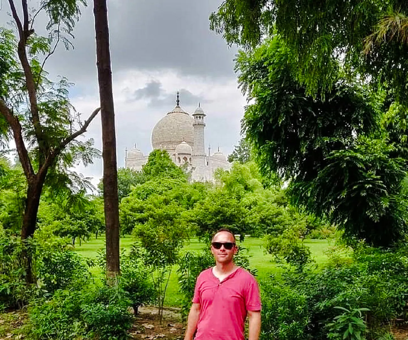 Taj Mahal dome visible through lush greenery in Agra during a guided tour.