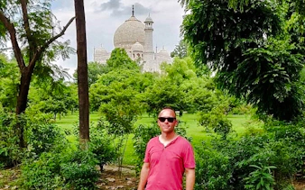 Taj Mahal dome visible through lush greenery in Agra during a guided tour.
