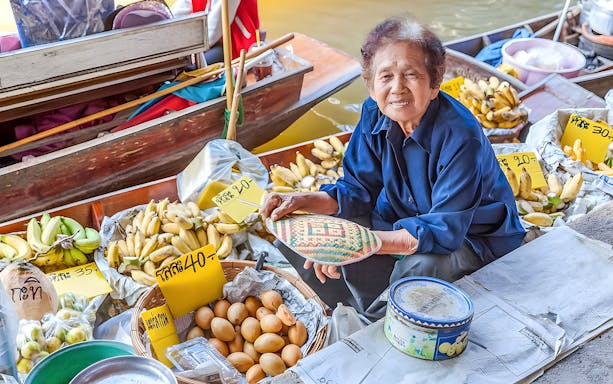 Vendor selling bananas and eggs at Damnoen Saduak Floating Market, Thailand.