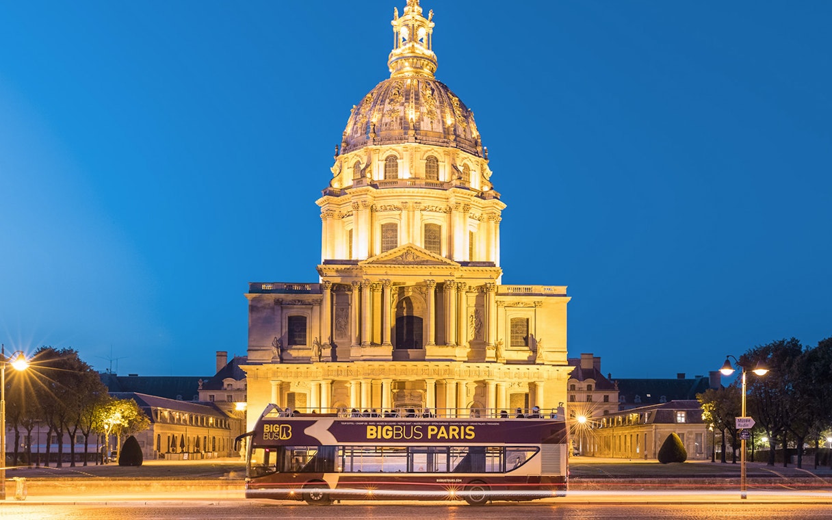 Open-top tour bus in front of Les Invalides, Paris at night.