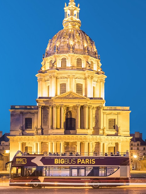 Open-top tour bus in front of Les Invalides, Paris at night.