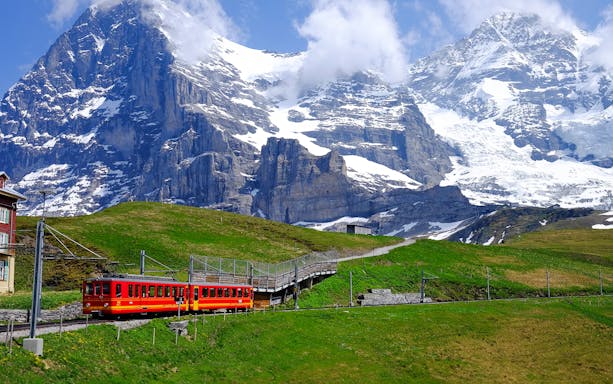 Jungfraujoch train traveling through snowy Swiss Alps with mountain peaks in the background.