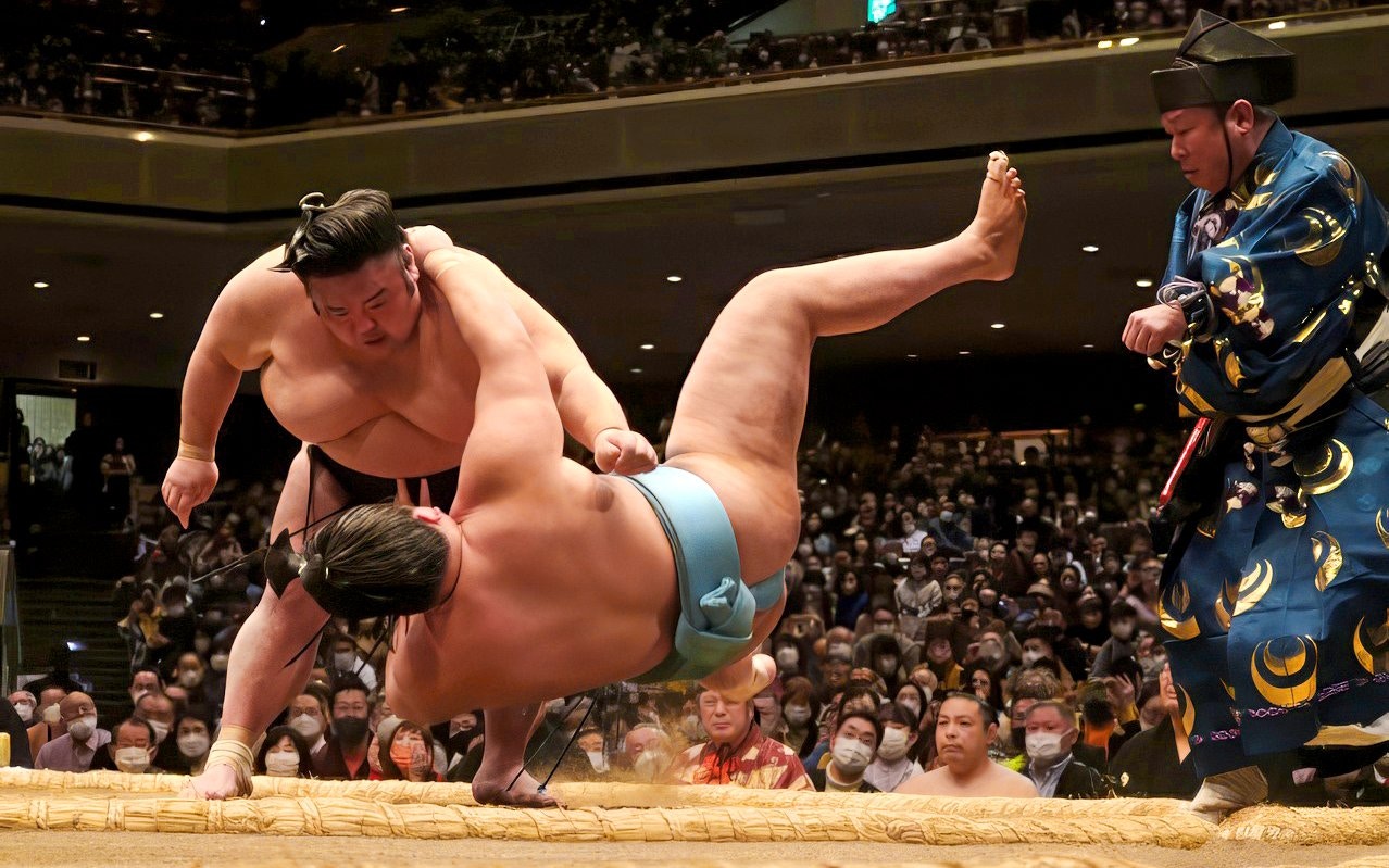 Sumo wrestler executing a move against opponent in a Japanese arena.