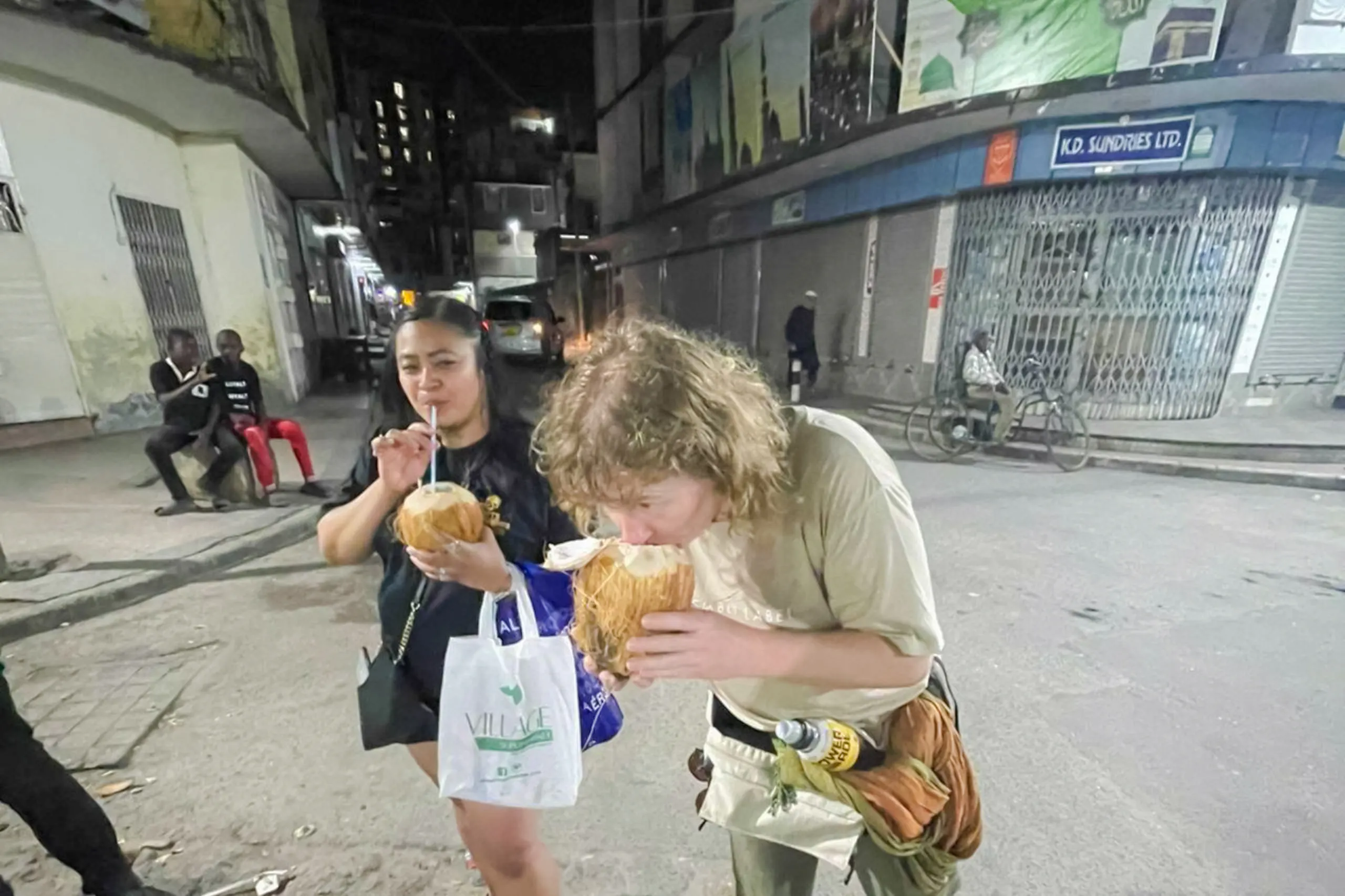 Tourists enjoying fresh coconuts during a night walk in Dar es Salaam Old Town, Zanzibar.
